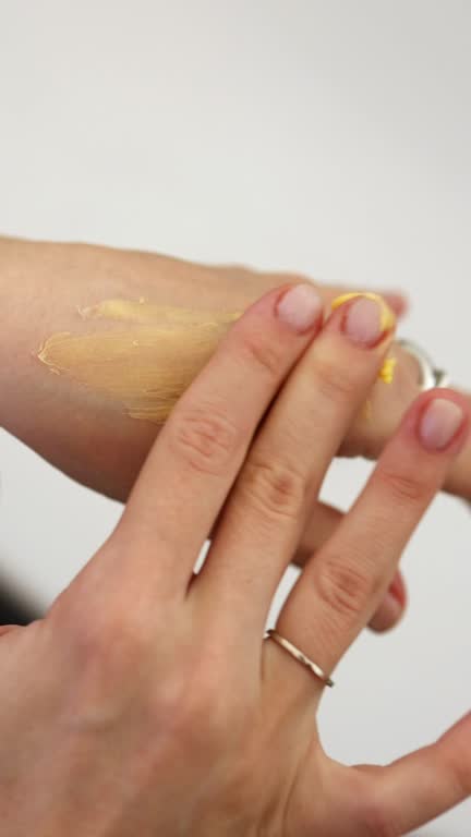 the girl smears yellow cream on her hand. vertical video. rubbing the cream on the hands. close-up of hands. vertical video