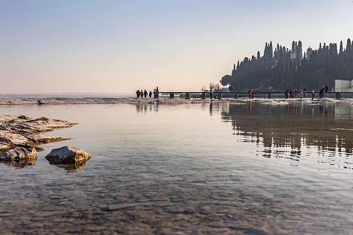 A stunning landscape photo of a rocky beach in Sirmione, with the clear waters of Lake Garda in the background