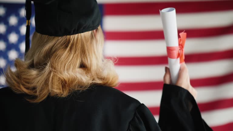 Graduate with a diploma against the background of the U.S. flag. View from behind