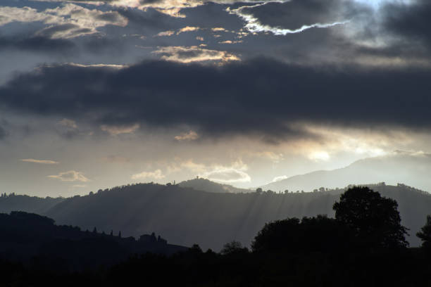 Backlit view of trees and hills under a cloudy sky