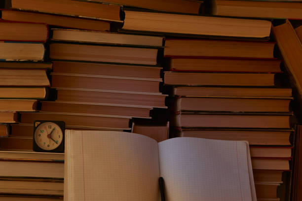 A notebook and a clock with folded books in the background, a symbol of knowledge and education. Human intelligence, learning, and knowledge.