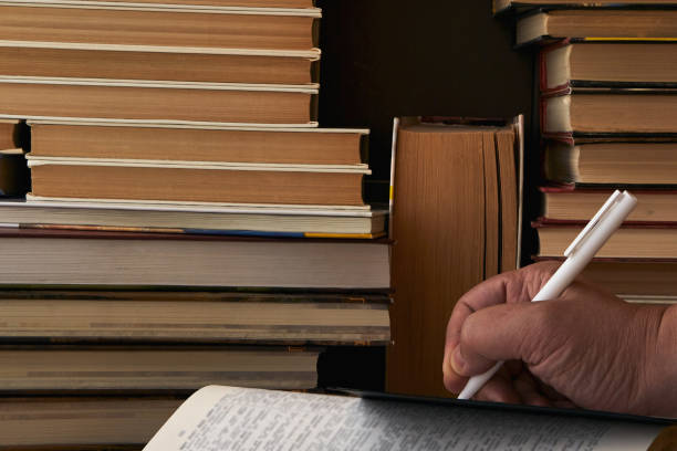 istock A hand with a pen writes in a notebook among the books. Human intelligence, learning, and knowledge. 2075949503