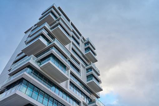 Towering contemporary building in city against cloudy sky, Modern architecture exterior with balconies and glass windows.