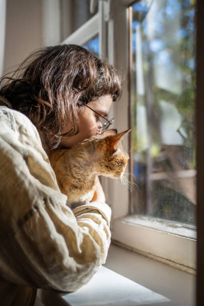 istock Caring pet lover cuddling beloved breed cat Devon Rex sitting on windowsill looking at window 2075955410
