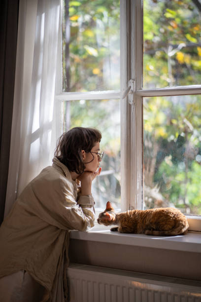 istock Depressed woman thinking about troubles sadly looking at window curious cat trying support owner. 2075955418