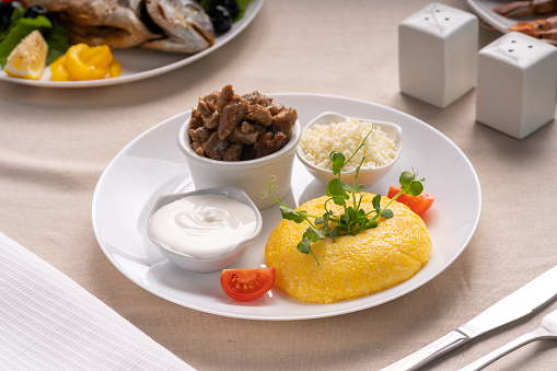 Delicious polenta with cheese, stew meat and sour cream on white plate serving on table. Traditional romanian healthy food. Above view.