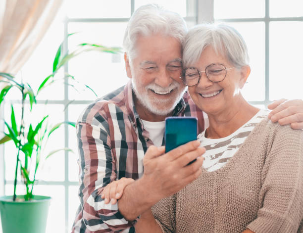 istock Video call concept. Happy bonding senior couple sitting on sofa, using smartphone technology for online webcam connection, enjoying carefree moments together with distant family 2075968044