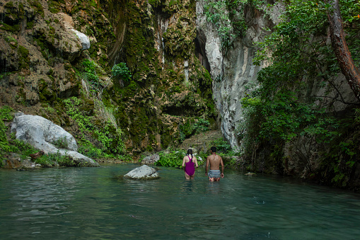 Heterosexual couple on eco-adventure trip entering natural pit cave entrance between stalactites natural rock formation