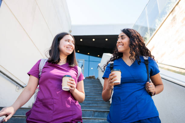 Two young hardworking latin female nurses talking with cup of coffee after work. Female Healthcare workers leaving hospital