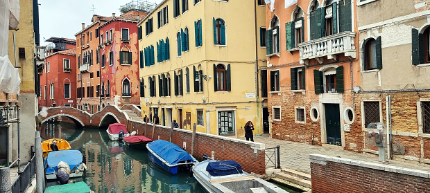 It's winter in Venice, and life is much quieter. Boats are stored along one of the smaller canals, and  people walk among some old buildings.