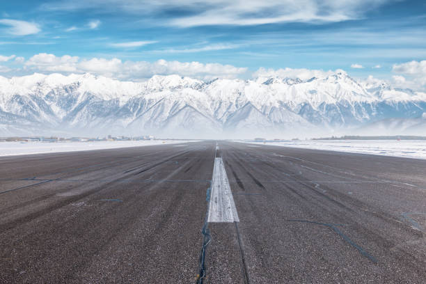 leere start- und landebahn des flughafens an einem wintertag vor dem hintergrund hoher, schneebedeckter berge - airfield mountain snow airport stock-fotos und bilder