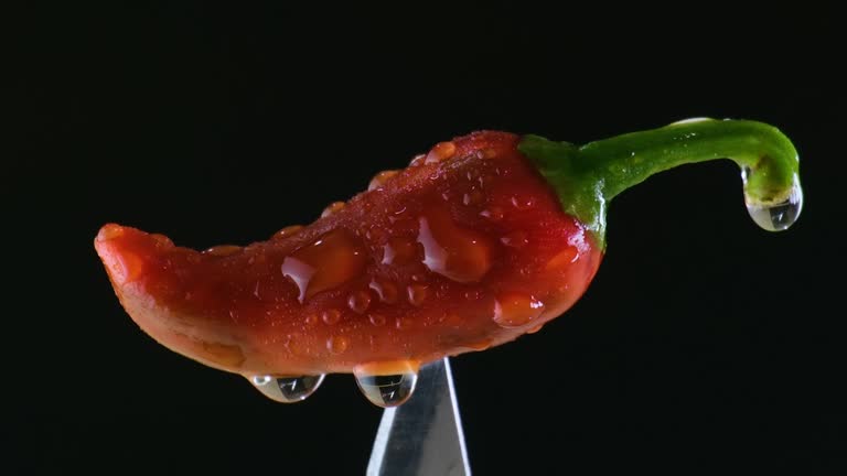 Water getting sprinkled on a red chilli on top of a knife. Closeup shot.