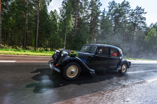 Vintage wedding car in motion on a sunny summer day after rain