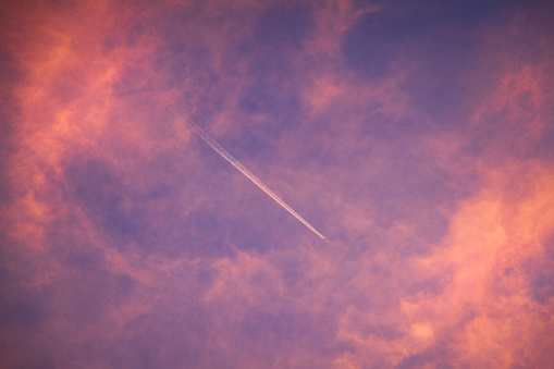 Plane flying high in a pink cloudy sunset sky with a vapor trail