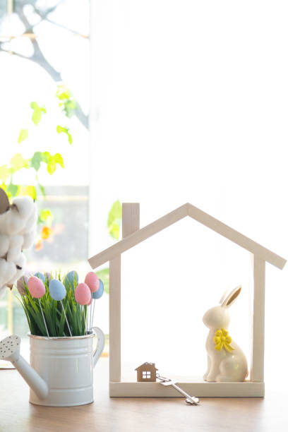 istock Key and tiny house of cozy home with Easter decor with rabbit and eggs on table of kitchen. Building, design, project, moving to new house, mortgage, insurance, rent and purchase real estate 2076140232