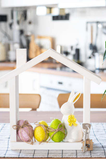 istock Key and tiny house of cozy home with Easter decor with rabbit and eggs on table of kitchen. Building, design, project, moving to new house, mortgage, insurance, rent and purchase real estate 2076140703