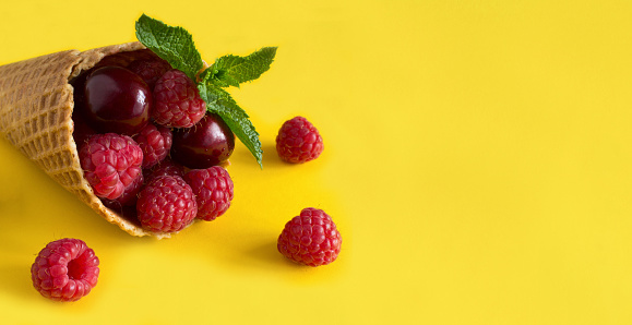 Ice cream cone with raspberries and cherry on the yellow background. Copy space. Close-up.