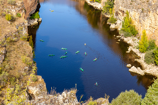 Hoces del Rio Duraton Nature Reserve (Parque Natural de las Hoces del Río Duratón) with limestone vertical cliffs, blue water and colorful kayaks floating.