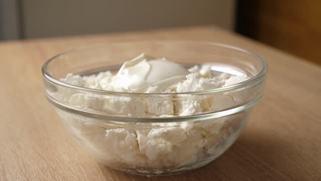 Sour cream is added to sour milk cheese and mixed.