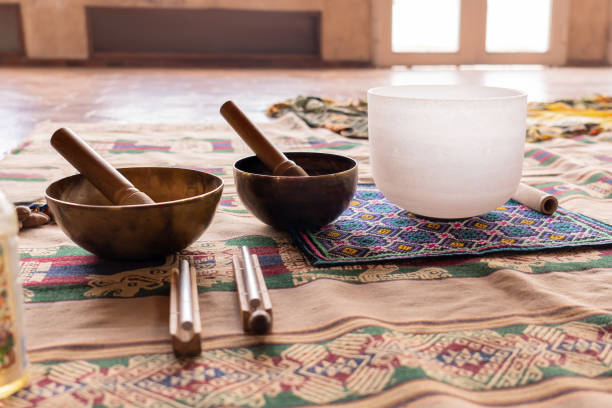 Instruments producing harmonic sounds, such as Tibetan and quartz singing bowls, placed on a blanket, prepared for a sound meditation, illuminated by bright light streaming in through a large window.