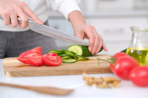 istock Woman cutting fresh cucumber and tomatoes at table in a light kitchen, closeup 2076212681