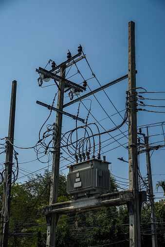 A power line pole with a transformer on top. The pole is surrounded by trees. The sky is clear and blue