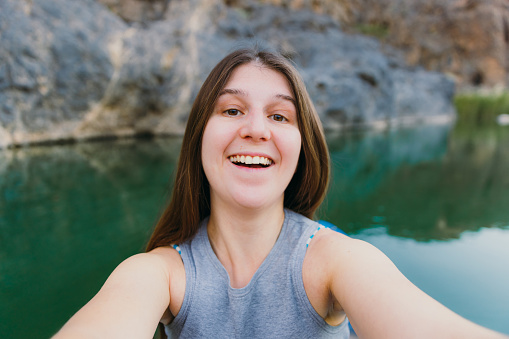Smiling female with long hair taking photo of herself during kayaking in the river hidden In the picturesque canyon in Oman