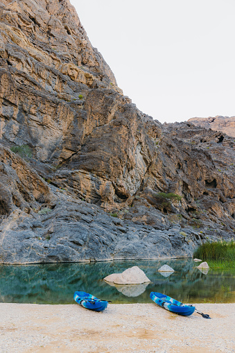 Scenic view of two blue kayak boats by the river hidden in the picturesque canyon in the mountains of Oman, Middle East