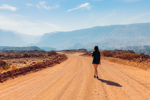 Middle Eastern female walking to her car on the desert road in the mountain range with picturesque view in Oman