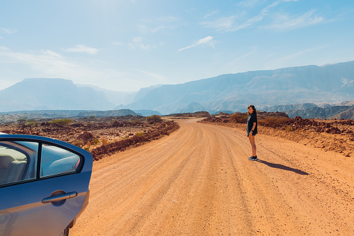 Middle Eastern female walking to her car on the desert road in the mountain range with picturesque view in Oman