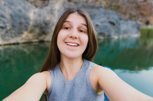 Smiling female with long hair taking photo of herself during kayaking in the river hidden In the picturesque canyon in Oman