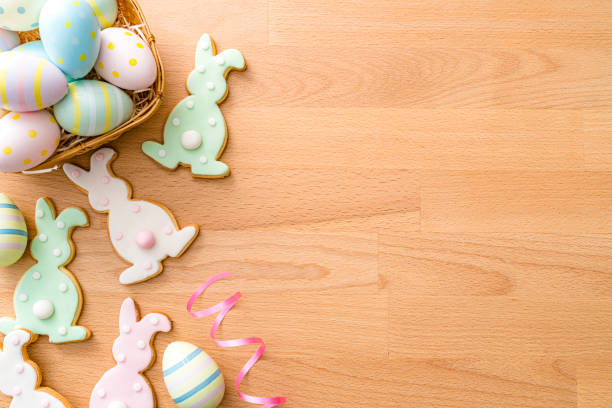 Overhead view of Easter Bunny cookies and Easter Eggs arranged at the left of a wooden table. Copy Space . High resolution 42Mp studio digital capture taken with SONY A7rII and Zeiss Batis 40mm F2.0 CF lens