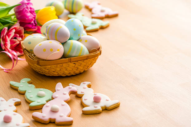 Overhead view of Esater Bunny cookies and Easter Eggs arranged at the left of a wooden table. Copy Space.