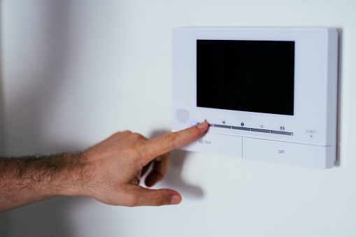 Man finger pressing a button on a wall-mounted home security system, emphasizing safety in residential spaces