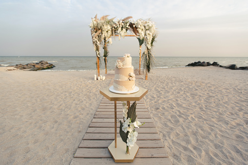 Wedding cake at a beach wedding on the background of a beautiful arch for an exit ceremony.