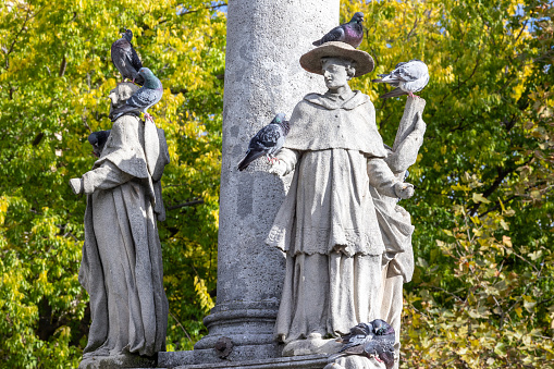 18th century statues, part of 18th century plague column on public square in Bratislava with several wild pigeons sitting on their heads