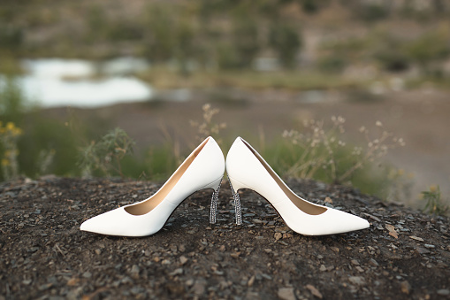 Women's wedding shoes on the ground against the background of the lake.