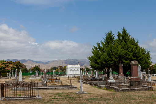 A cemetery with many graves and a large stone wall. The cemetery is empty and quiet. Scene is somber and peaceful