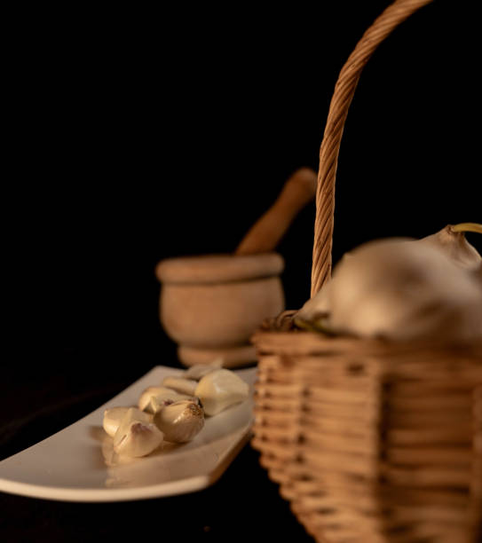 A basket full of garlic heads and next to it a wooden almirez and a tray with peeled cloves