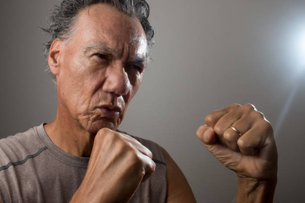 An elderly man in his office is showing a fist.