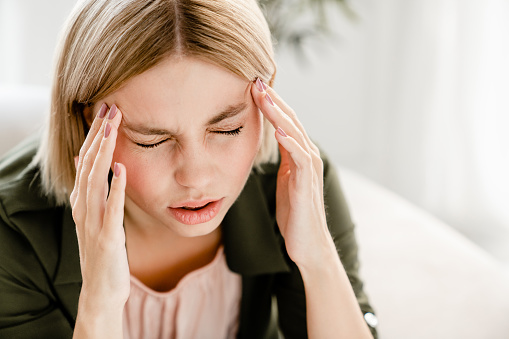 Sad caucasian woman having migraine rubbing temples. Young female girl suffering from headache, period crumps, having problems, being fired, crying at home