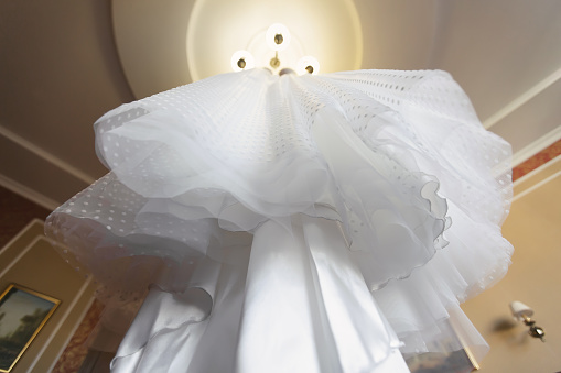 a view of a wedding dress from below with jagged edges, layers hanging from an iron rod detail on a chandelier