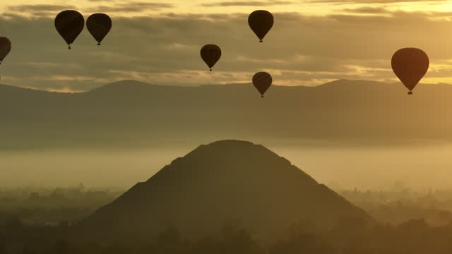 Pyramid structure and Hot-air balloons, backlit by a hazy sunrise sky - Aerial view
