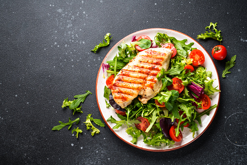 Healthy food. Chicken steak BBQ grill meat with fresh salad on black background. Top view.