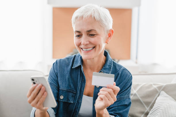 istock Friendly mature woman using credit debit card and cellphone for e-banking e-commerce at home. 2076410825