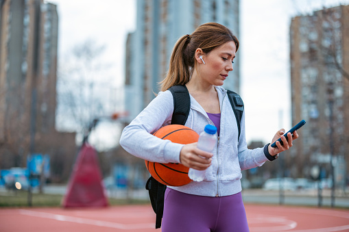 Holding her bag, a woman walks towards the basketball court, displaying her commitment to partake in basketball-related activities