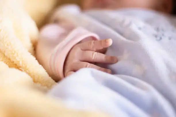 Close up of caucasian newborn baby sleeping in cozy carrycot with colorful blankets. Selective focus on her delicate, tiny hand.