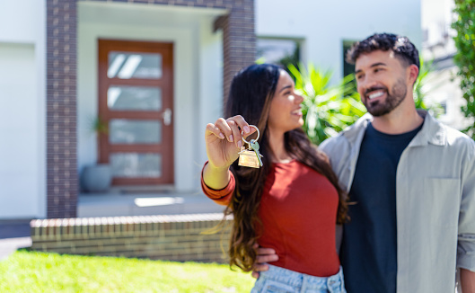 happy woman and man, holding keys from new first house, young family celebrating moving day, satisfied customers couple purchase real estate, mortgage and relocation concept. The building can be seen in the background