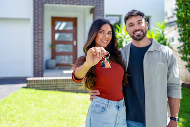 happy woman and man, holding keys from new first house, young family celebrating moving day, happy woman and man, holding keys from new first house, young family celebrating moving day, satisfied customers couple purchase real estate, mortgage and relocation concept. The building can be seen in the background happy family with key of their new house stock pictures, royalty-free photos & images