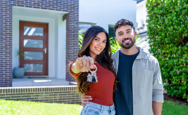 happy woman and man, holding keys from new first house, young family celebrating moving day, happy woman and man, holding keys from new first house, young family celebrating moving day, satisfied customers couple purchase real estate, mortgage and relocation concept. The building can be seen in the background happy family with key of their new house stock pictures, royalty-free photos & images